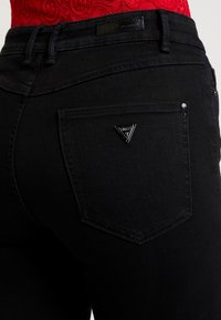 Svarta denimjeans med en liten svart triangulär logotyp på bakfickan, med subtila sömnadsdetaljer och en rak passform.