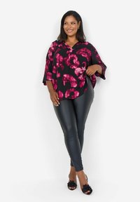 Haut noir avec un motif floral rose, coupe ample et manches larges, associé à des leggings noirs serrés et des chaussures ouvertes noires.
