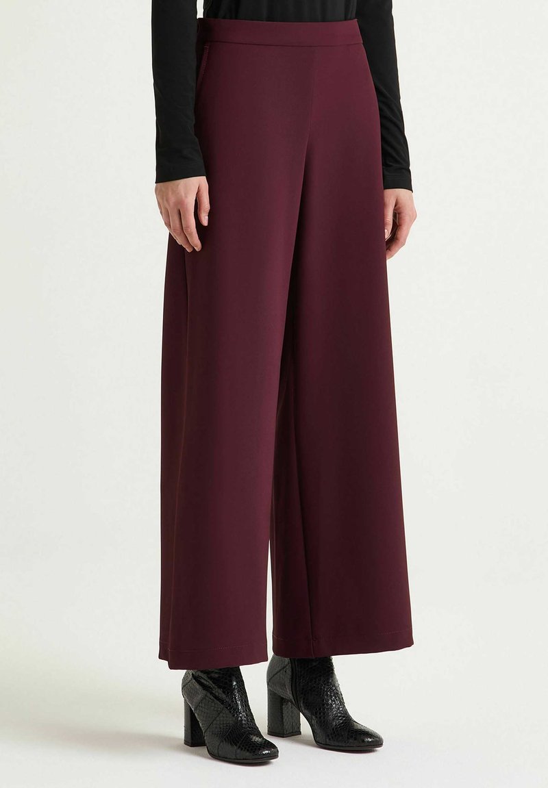 Pantaloni a gamba larga in tessuto color bordeaux, con vita alta e texture liscia. Abbinati a tacchi neri con motivo testurizzato.