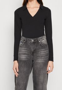 Svart långärmad body med v-ringning och krage som är kombinerad med högmidjade, blekta grå denimjeans med avslappnad passform och synliga sömmar.