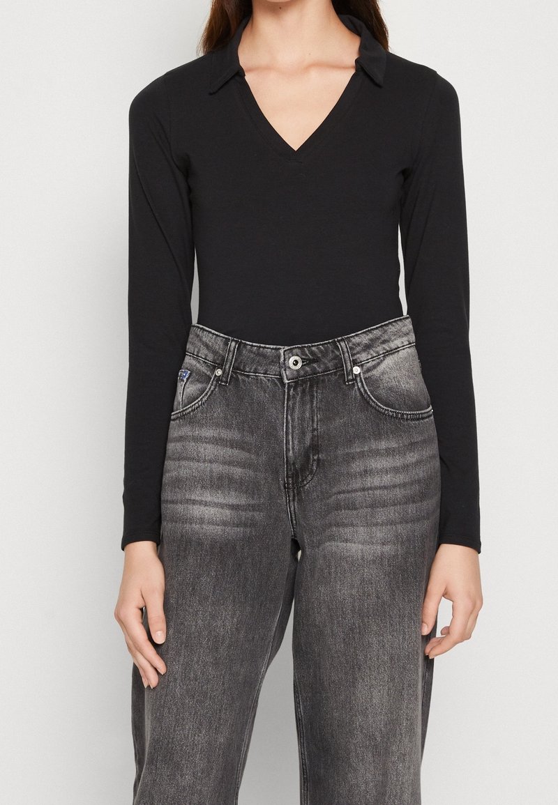 Svart långärmad body med v-ringning och krage som är kombinerad med högmidjade, blekta grå denimjeans med avslappnad passform och synliga sömmar.