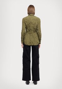 Wrinkled olive green blouse with a collar, fitted waist, and long sleeves paired with black wide-leg cargo pants featuring side pockets.