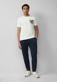 Witte katoenen t-shirt met een blauwe grafische print op de linkerborstzak. Gecombineerd met marineblauwe tapered broek en lichtgekleurde sneakers.