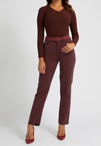 Maglietta a maniche lunghe a costine color marsala con scollatura a V, abbinata a pantaloni marsala a vita alta, dotati di una cintura coordinata e décolleté a punta.