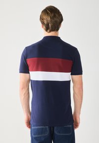 Marine-blå polo skjorte med røde og hvite horisontale striper på baksiden. Korte ermer, klassisk krage og mykt bomullsmateriale. Uformell passform.
