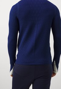 Navy blue sweater with a textured honeycomb pattern and long sleeves. Features a split hem and light blue striped accents at the cuffs.
