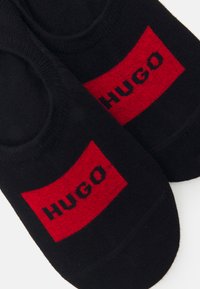 Juodos kulkšninių kojinių su raudonu stačiakampiu logotipu, ant kurio užrašyta žodis "HUGO" kontrastinga juoda spalva. Pagamintos iš minkštos, tamprios medžiagos.