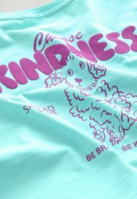 Camiseta de manga corta color verde menta con un gráfico morado de un perro esponjoso y el texto "Elige la amabilidad" y "Difunde amor". Textura suave.