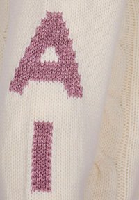 Primo piano di un tessuto a maglia crema con una grande lettera "A" rosa in rilievo ricamata sopra.