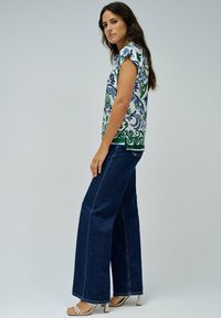 Top de manga corta con estampado floral en blanco, verde y azul, combinado con unos vaqueros de pierna ancha de denim oscuro y tacones beige con tiras.