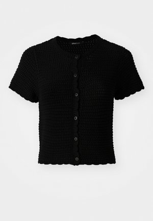 Must have lühikeste varrukatega must kudumiskardigan, millel on ümar kaelus, skaalakujuline äär ja kuus musta nuppu ees.