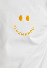Hvit t-skjorte med en gul smilefjesgrafikk, som har to sirkulære øyne og teksten "BLUE MARBLE" i en buet arrangement under smilet.
