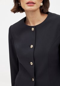 Czarna dopasowana marynarka z okrągłym dekoltem, sześcioma złotymi guzikami i dopasowanym krojem, o gładkiej fakturze.