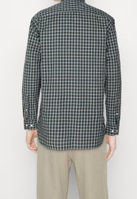 Camisa a cuadros en azul oscuro, beig y verde. Mangas largas con puños abotonados, bajo recto y diseño en la parte trasera. Tejido de algodón.