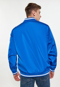 Jasne modré ľahké sako s hladkou textúrou, ribovaným bielym golierom a manžetami, vybavené zväčšeným lemom a kontrastnými akcentmi.