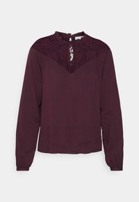 Blusa bordeaux con maniche lunghe, dettagli in pizzo sulle spalle e sul collo, e una leggera arricciatura al colletto. Tessuto dalla consistenza liscia.
