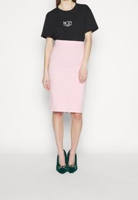 Black t-shirt with white logo, paired with a fitted pink pencil skirt, and green textured heels featuring a chain accent.