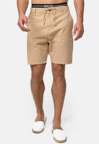 Beige stribede shorts med snøre i livet, to forlommer og en afslappet pasform. Sammen med hvide slip-on sko.