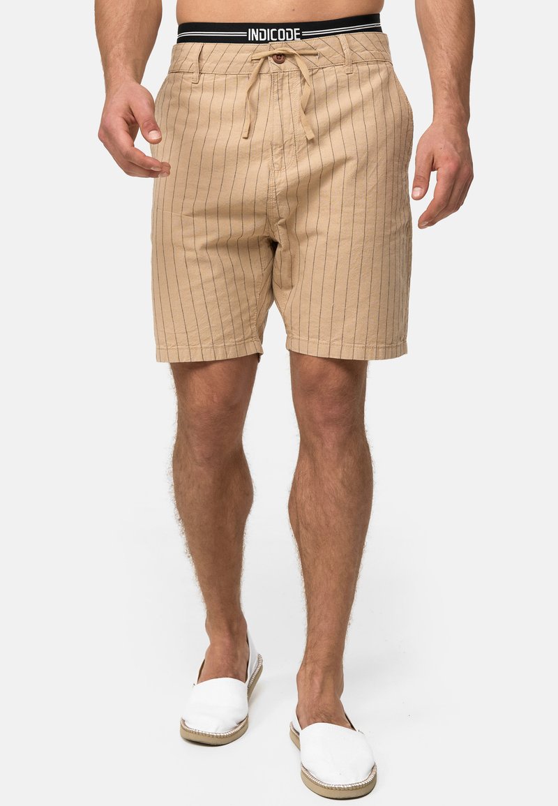 Beige stribede shorts med snøre i livet, to forlommer og en afslappet pasform. Sammen med hvide slip-on sko.