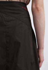 Czarna spódnica z wysokim stanem, o fakturowanej powierzchni i czerwonym haftowanym detalu przy pasie. Zaprojektowana w kształcie rozszerzanym.