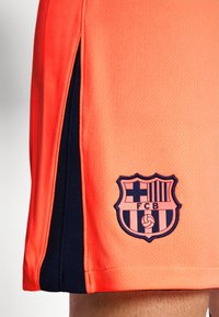Oranzid sporditrendid navy siniste külgpaneelidega, millel on sinise ja punase värviga FC Barcelona logo brodeeritud. Tekstuurne materjal koos jagatud servaga.