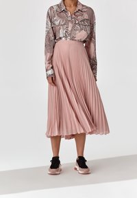 Gonna plissettata rosa chiaro abbinata a una blusa a maniche lunghe con motivo floreale. Sneakers sportive nere e rosa completano l'outfit.