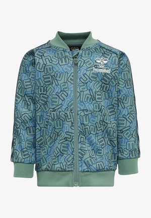Zielona kurtka zapinana na zamek błyskawiczny z powtarzającym się wzorem niebieskich i czarnych motywów, z ribbngowymi mankietami i kołnierzem, wykonana z gładkiego materiału.