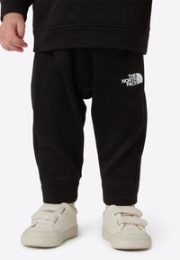 Pantaloni della tuta neri dal taglio comodo, con un logo bianco di The North Face sulla coscia sinistra. Abbinati a sneakers bianche con chiusura in velcro.