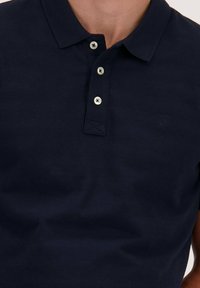 Marineblauwe polo-shirt van textuurstof, met een klassieke kraag, drie knopen sluiting en een klein logo op de borst.