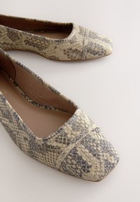 Paari lamedaid kingi beeži ja halli madunaha mustriga ning ruudukujuliste ninadega helel taustal.