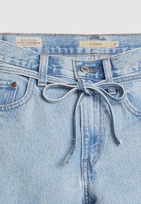 Ljust blå Levi's Premium jeans med ett knytbart tygbälte, metallknapp, bältesöglor och synliga märkningar för varumärke och storlek.