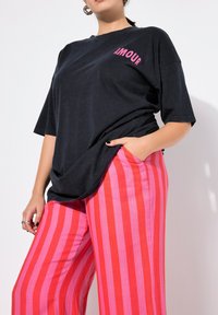 Zwarte oversized t-shirt met "AMOUR" in roze op de borst, gecombineerd met roze en rode verticaal gestreepte wijde broek met een losse pasvorm.