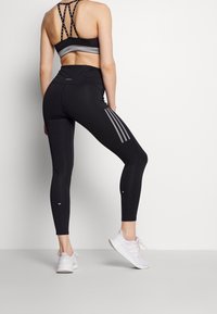 Czarne legginsy sportowe z szarymi akcentami, wykonane z elastycznego materiału; zestawione z dopasowanym biustonoszem sportowym z krzyżującymi się ramiączkami z tyłu.