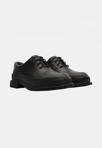 Chaussures noires en caoutchouc avec un design à lacets, bout arrondi, semelle texturée et bords surélevés. Finition lisse avec un minimum de détails.