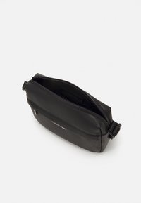 Černá kožená crossbody taška s texturovaným povrchem, zipovým uzavíráním, nastavitelným popruhem a embosovaným logem na přední straně.