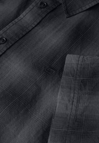 Svart vävd skjorta med en texturerad tyg med ett rutmönster, knäppt fram, och en liten broderad logotyp på bröstfickan.