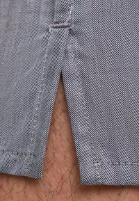 Shorts pour hommes à motif chevrons, avec des rayures bleues et blanches. Comprend une fente latérale, tissu texturé visible et coutures apparentes.