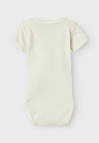 Bodysuit à manches courtes de couleur crème fabriqué en coton doux. Il présente un col rond et des boutons-pression en bas pour un habillage facile.