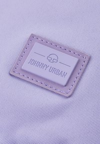 Ibolyaszínű, textúrált felületű anyagon egy téglalap alakú embléma látható, taupe színű hímzéssel, melyen "JOHNNY URBAN" felirat olvasható dombornyomott betűkkel.