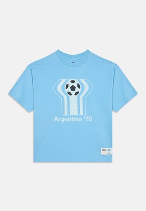 Lichtblauw T-shirt met een gestileerde voetbal en witte strepen, tekst vermeldt "Argentina '78" als verwijzing naar het WK voetbal van 1978.