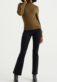 Olive green knitted sweater with a textured pattern, paired with black flared jeans and ankle boots, set against a plain background.