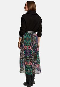 Maglione nero lavorato a maglia con collo a cascata, abbinato a una lunga gonna colorata e decorata con motivi verdi, viola e rosa.