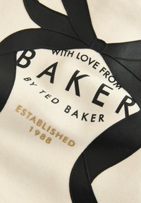 tissu crème avec des accents en faux cuir noir en forme de ruban, présentant un texte noir en gras "BAKER" et un texte doré "ÉTABLI EN 1988".