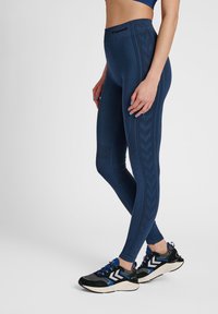 Marineblauwe legging gemaakt van rekbaar materiaal, met een textuurpatroon en hoge tailleband. Gecombineerd met zwarte en blauwe sportschoenen.