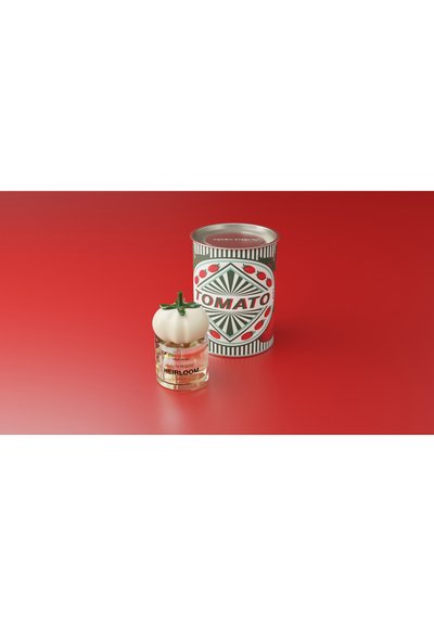 Tomatscentad parfymflaska med ett vitt tomatformat lock bredvid en dekorativ tomatsoppa-burk på en röd yta.