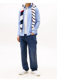 Camisa de botones azul claro, camiseta blanca debajo, vaqueros anchos azul oscuro, bufanda a rayas colgada alrededor del cuello, zapatillas blancas.