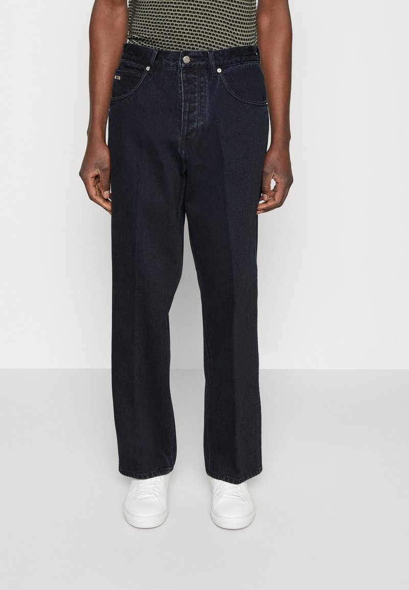 Mörk denim bredbenade jeans med midja som sitter något högre, med fem fickor och subtila sömnadsdetaljer. Bärs med vita sneakers.