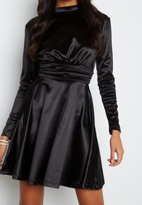 Robe en satin noir avec de longues manches, un corsage ajusté et une taille froncée, se déversant en une jupe évasée au tissu lisse.