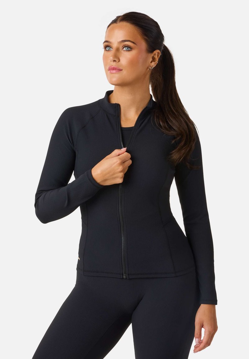 Svart zip-up jacka i ribbat material med hög krage och långa ärmar. Tight passform, ihopparad med matchande underdelar.