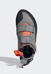 Sapatilha de escalada cinza com sola de borracha preta, detalhes em malha laranja e fechos de Velcro. Possui uma aba no calcanhar para facilitar o calce.